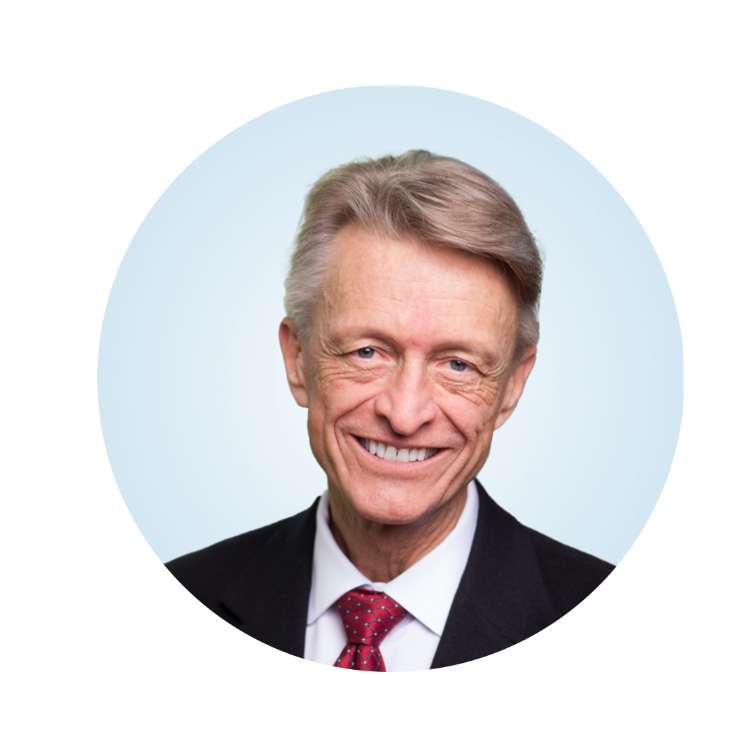 Head-and-shoulders portrait of a smiling older man with light gray hair, wearing a dark suit, white shirt, and red tie, against a light blue circular background.