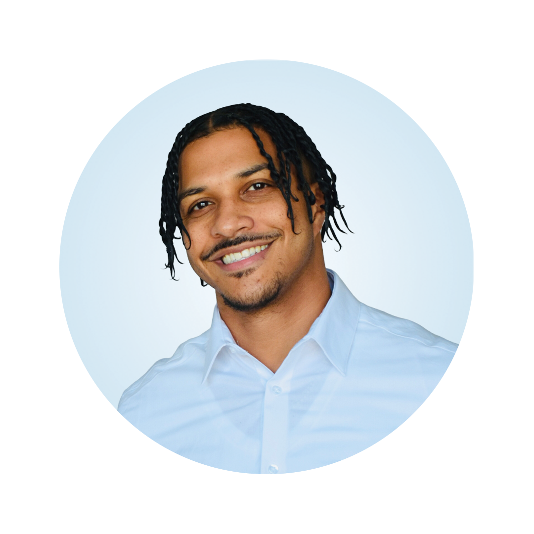 Professional headshot of a smiling man with braided hair wearing a light blue dress shirt against a light blue circular background.