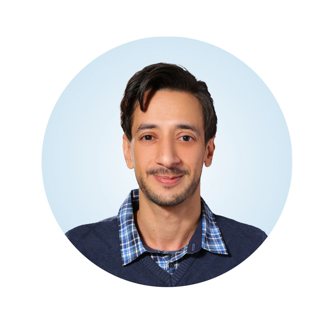 Head-and-shoulders portrait of a smiling man with short dark hair, wearing a blue sweater over a plaid shirt, against a light blue circular background