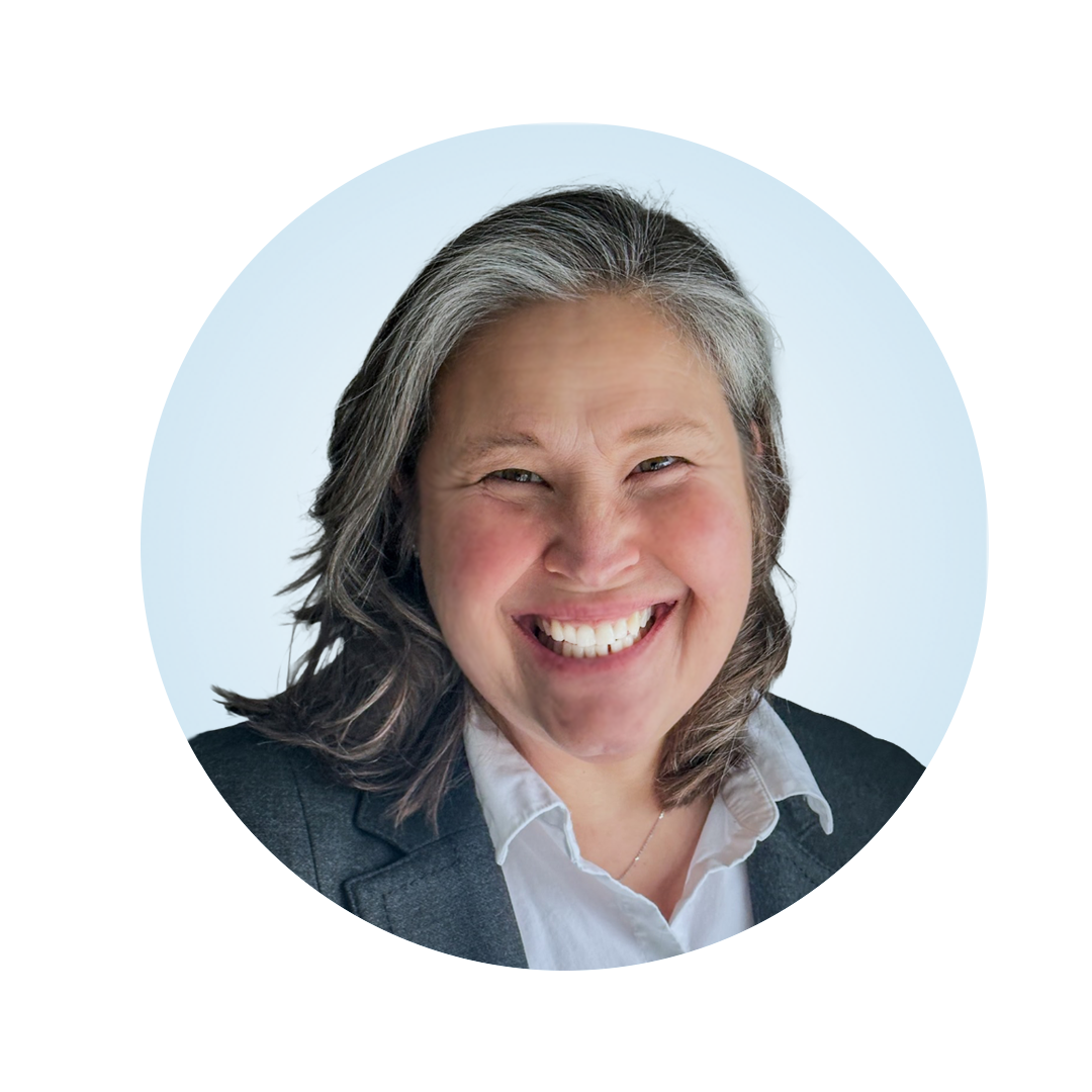 Smiling caucasian female, wearing a gray jacket with a white buttoned shirt centered in a light blue circle.