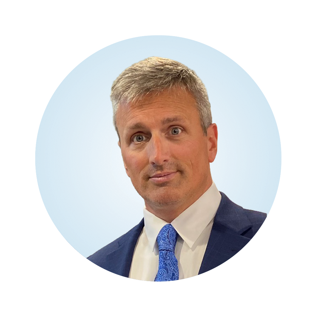 Professional headshot of a man with short gray hair wearing a blue suit and patterned tie against a light blue circular background.