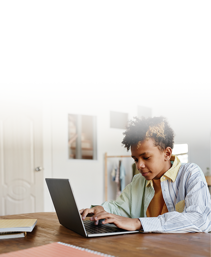 Student focused on typing on a laptop at a table in a home learning environment, working independently on schoolwork.