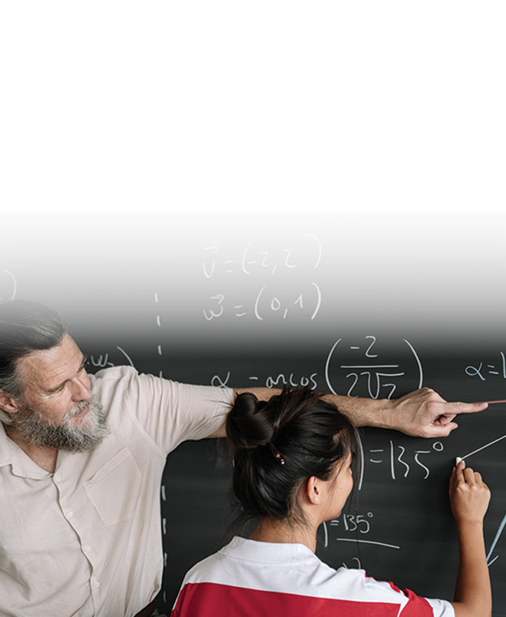 Teacher guiding a student at a chalkboard, pointing to a math equation while the student writes and solves a problem.
